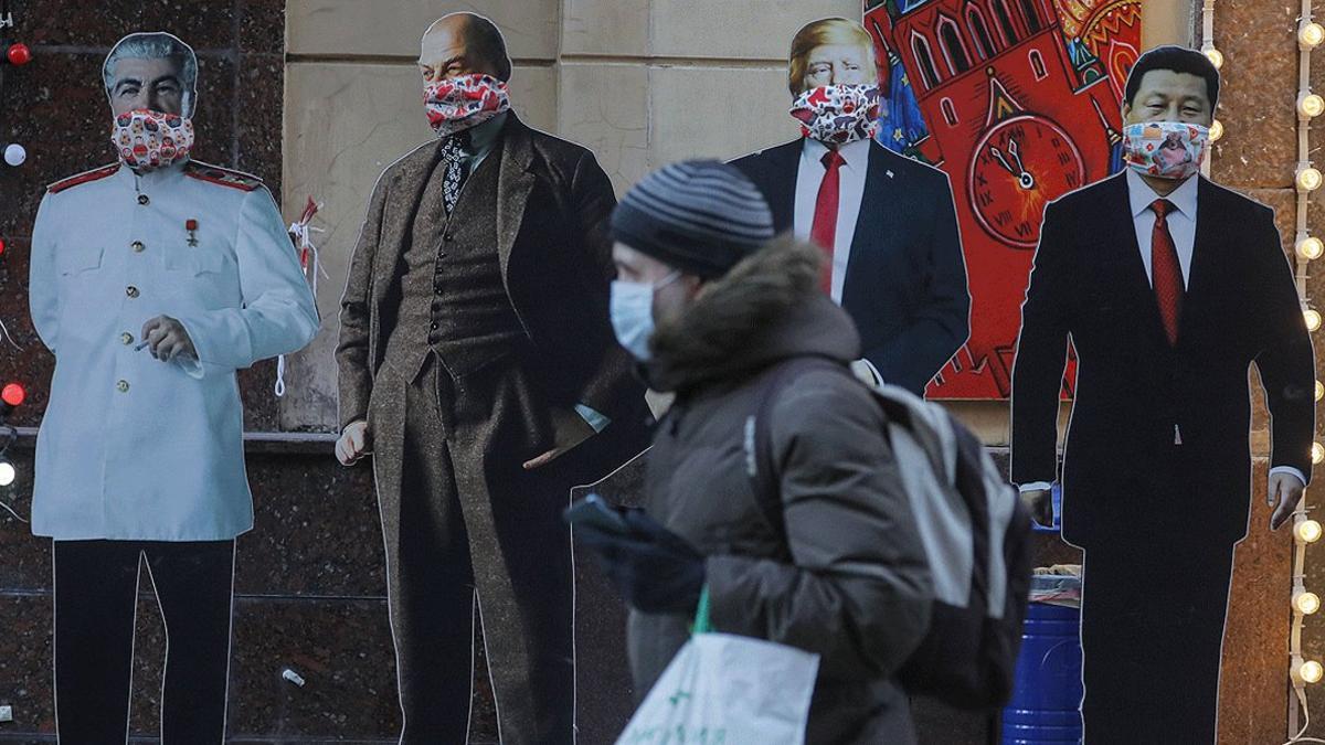 Una mujer pasa por delante de varias figuras de cartón de Stalin, Lenin, Xi Jinping y Donald Trump ataviadas con mascarillas, junto a una tienda de suvenires en Moscú, el 24 de marzo