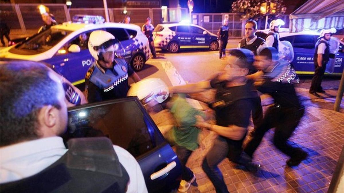 Policías de uniforme y de paisano intentan introducir en un coche a un detenido tras la pelea mortal.