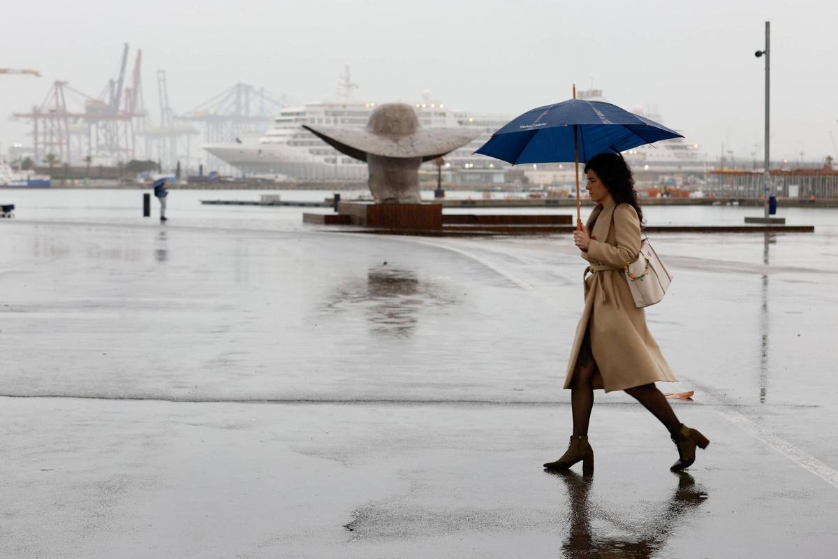Lluvia este viernes en València con una mujer paseando por el puerto.