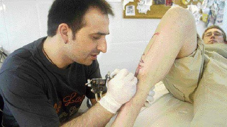 Un profesional realiza un tatuaje en una pierna a un joven en una tienda especializada de Vigo. / CARLOS PEREIRA