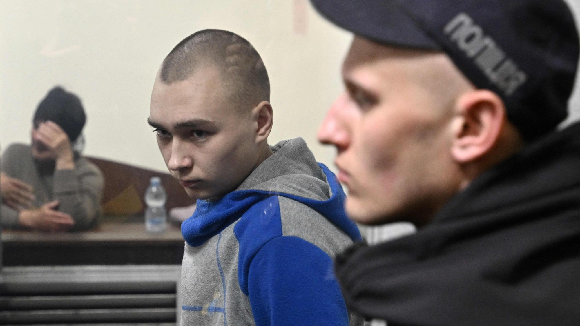 Russian soldier Vadim Shishimarin (C) looks on from the defendant's box at the opening of his trial on charge of War crimes for having killed a civilian, as his widow Kateryna Shelipova (L) reacts, in the Solomyansky district court in Kyiv on May 18, 2022. - The captured soldier is accused of killing a 62-year-old civilian -- allegedly on a bicycle -- near the village of Chupakhivka in the northeastern Ukraine Sumy region on February 28, in the first days of the Russian's offensive. Shishimarin pleaded guilty and is facing possible life imprisonment in Kyiv. (Photo by Genya SAVILOV / AFP)
