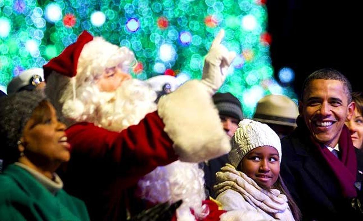 El president nord-americà, Barack Obama, la mare de la primera dama, Marian Robinson, i la seva filla Sasha participen amb un home disfressat de Santa Claus en la cerimònia d’il·luminació de l’Arbre de Nadal Nacional, a prop a la Casa Blanca, a Washington D.C. (Estats Units).