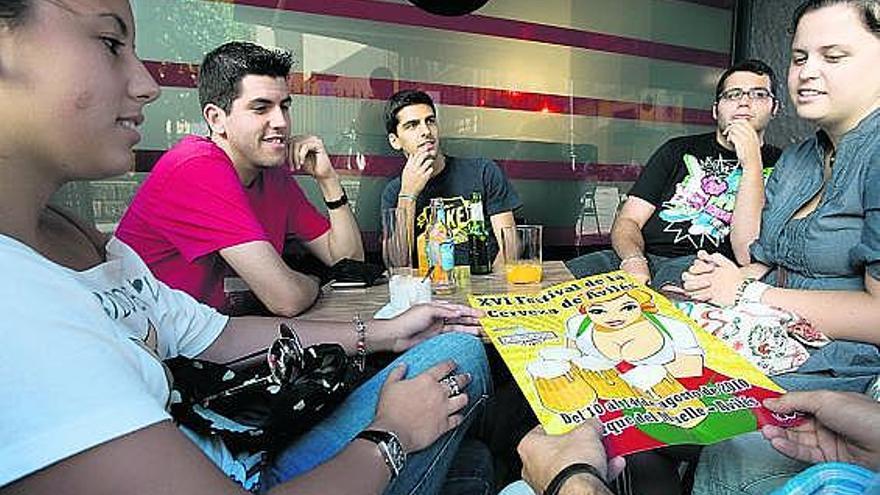 Un grupo de jóvenes, observando el cartel del Festival de la Cerveza, ayer, en una terraza de Avilés.