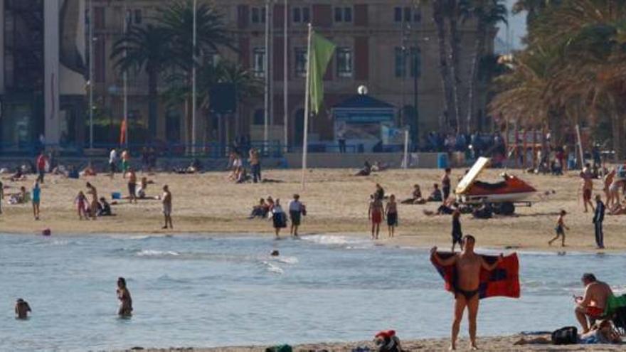 Un bañista se seca tras salir del agua mientras unas jóvenes se bañan en la playa alicantina de El Postiguet ayer.