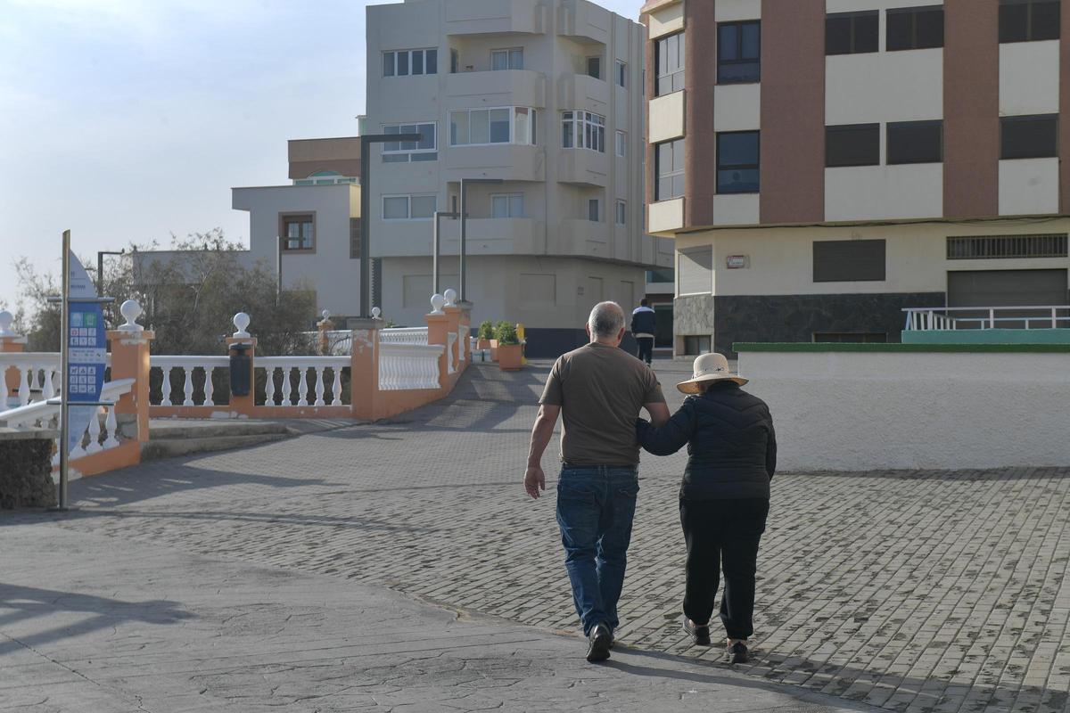 Dos personas pasean por la avenida que une Melenara y Salinetas, salpicada de viviendas