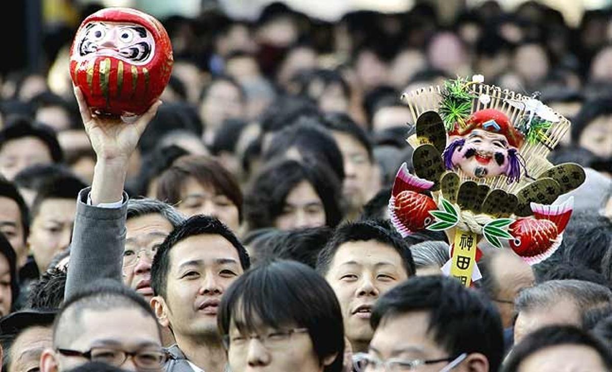 Dos homes de negocis japonesos sostenen un ninot daruma i un rasclet de bambú decorat, mentre fan fila per resar al temple Kanda Myojin de Tòquio (Japó).