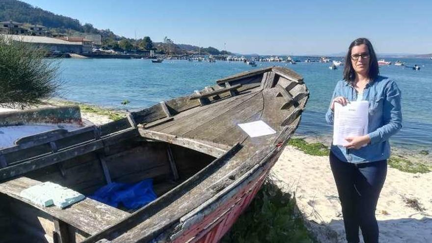 La concejala de Medio Ambiente de Cangas, Tania Castro, colocando el miércoles un cartel de aviso para la retirada de la embarcación en la playa de Vilariño. // G.N.