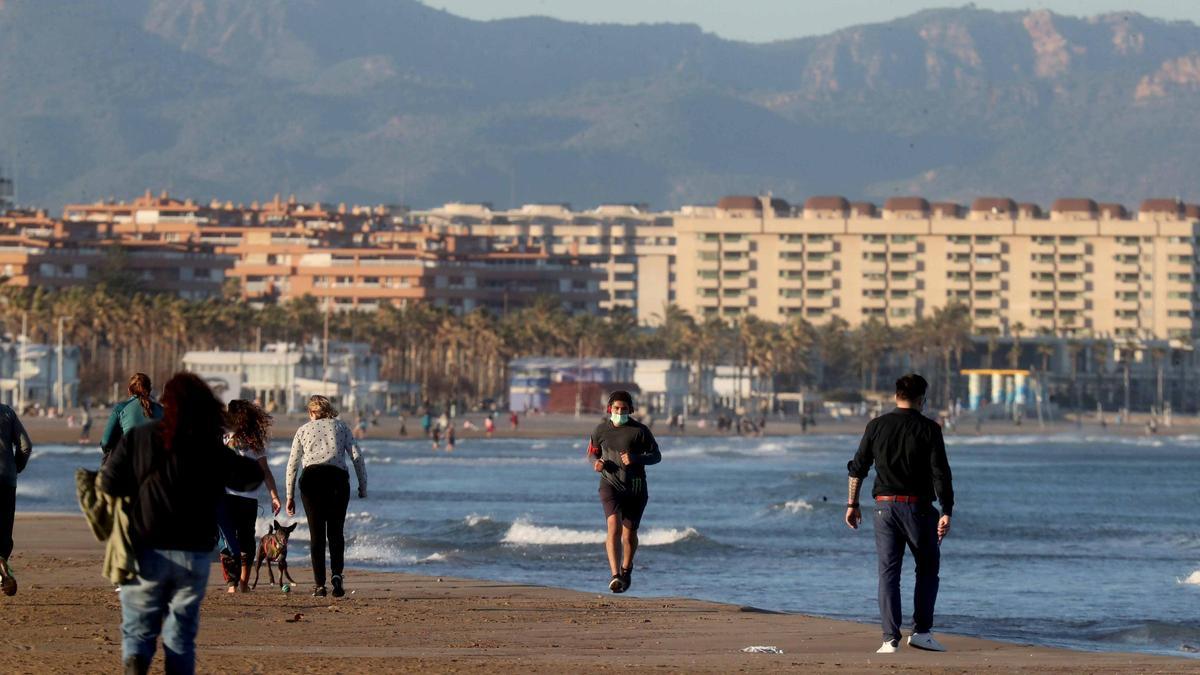 Varias personas pasean con mascarilla por la playa en València.