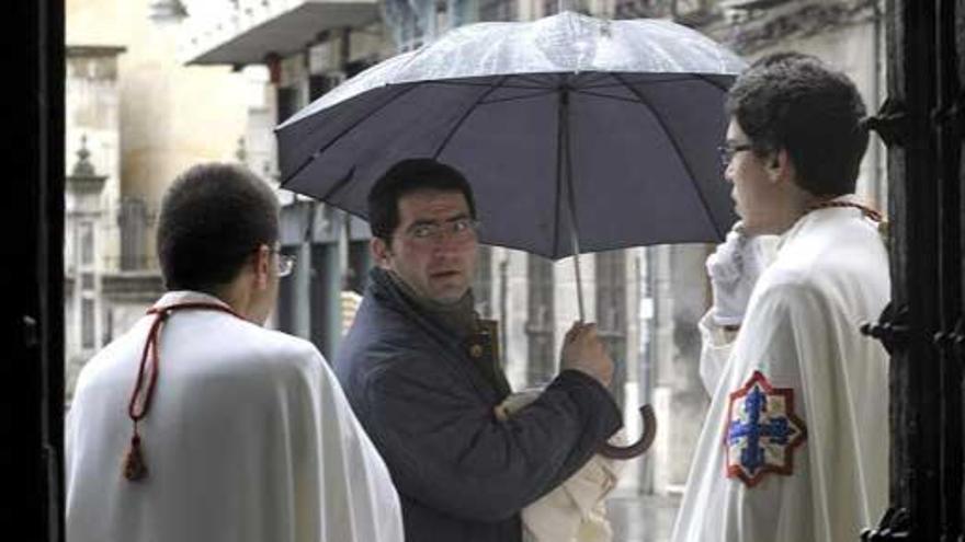 Un ciudadano, paraguas en mano, conversa con dos cofrades en Valladolid.