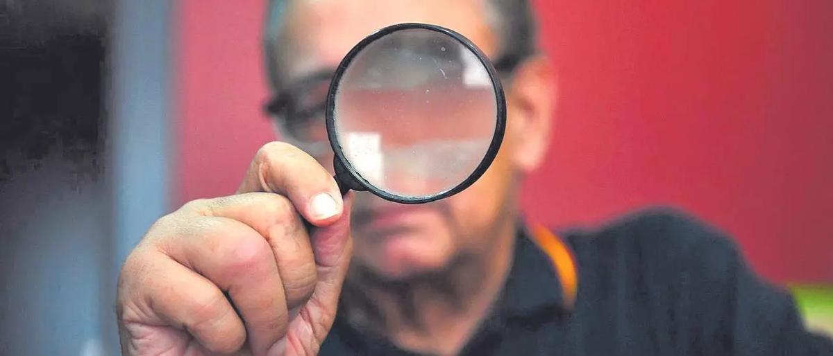 Un detective oculta su rostro bajo una lupa.