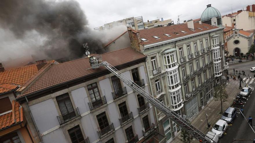 Los bomberos, durante la labor de extinción del fuego de Uría, en una imagen tomada desde la trasera del edificio, en la calle Melquiades Álvarez