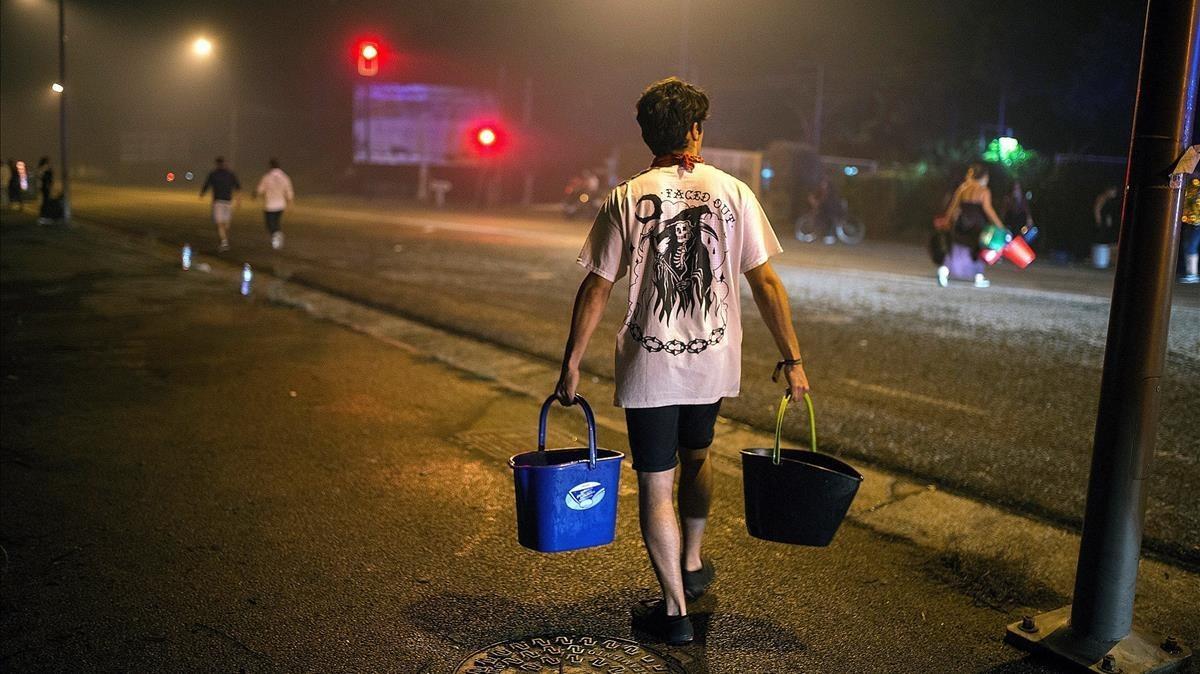 Un hombre porta dos cubos de agua para ayudar a sofocar uno de los focos declarados en el centro de Vigo.