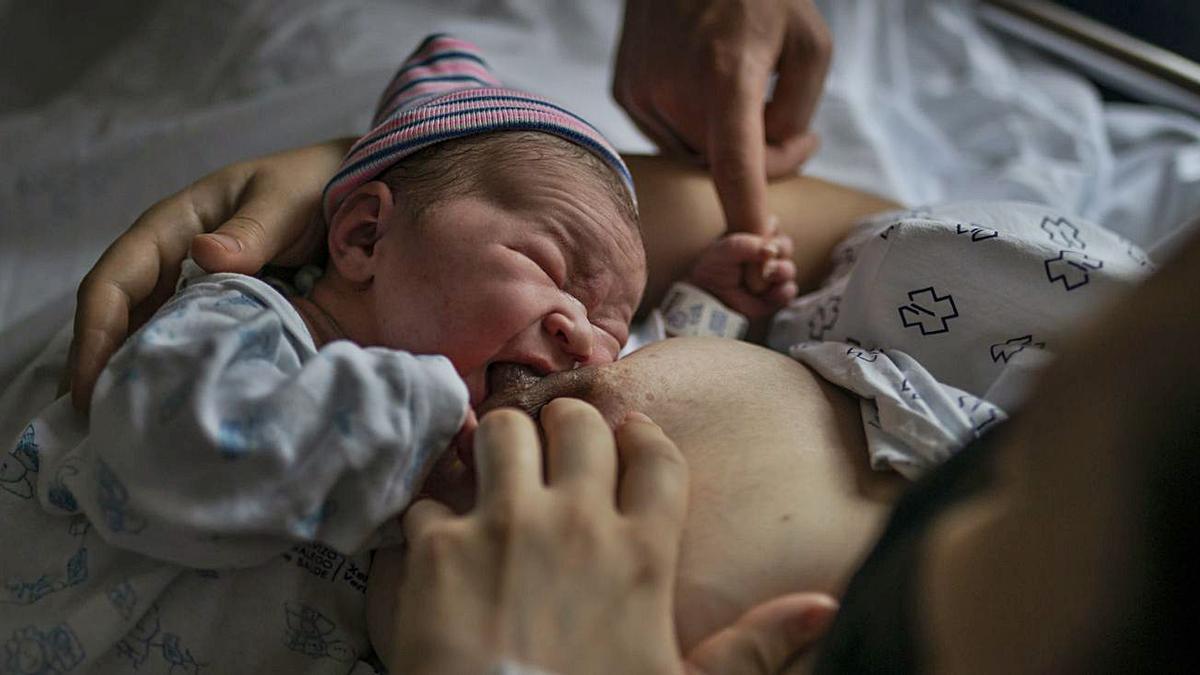 Una mujer con mascarilla da el pecho a su hijo en un hospital del Sergas.  | // BRAIS LORENZO