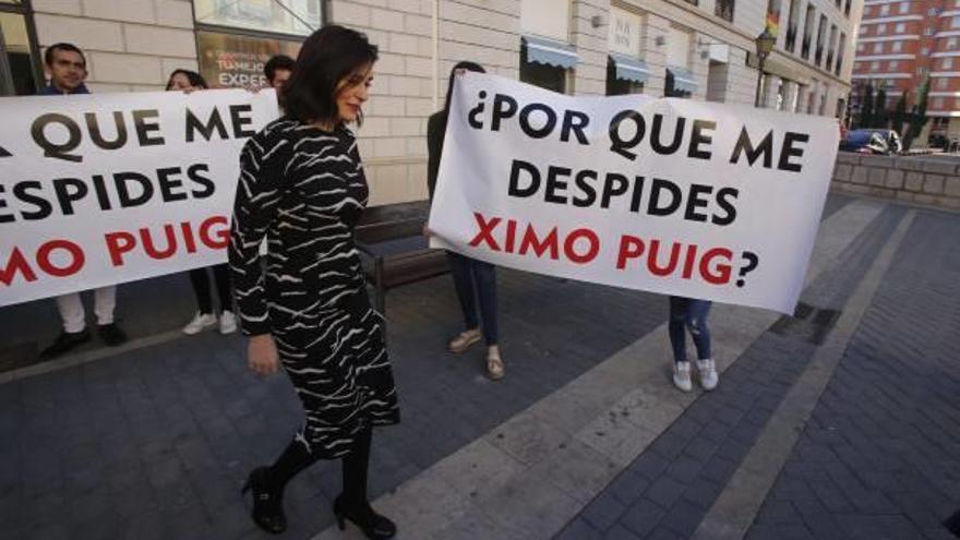La exconsellera Carmen Montón pasa ante una pancarta contra los despidos días antes de la reversión.