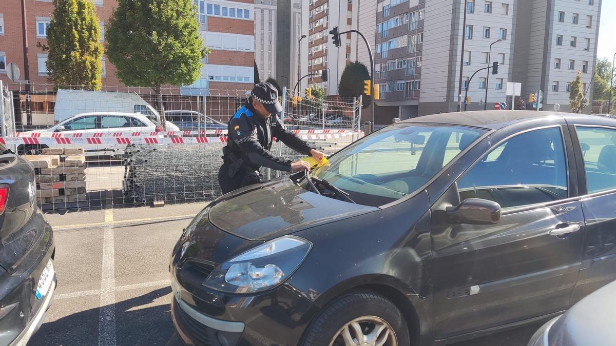 Un agente de la Policía Local colocando avisos en los parabrisas de los coches aparcados.