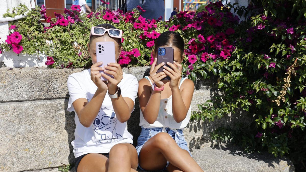 Dos niñas, mirando las pantallas de sus móviles.