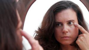 Una mujer observa el contorno de sus ojos frente a un espejo.