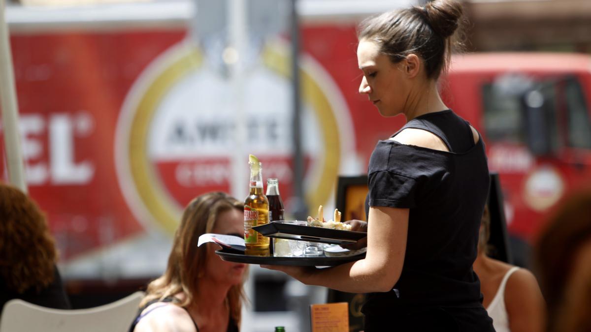 Una camarera sirve unas mesas en la terraza de una cafetería.