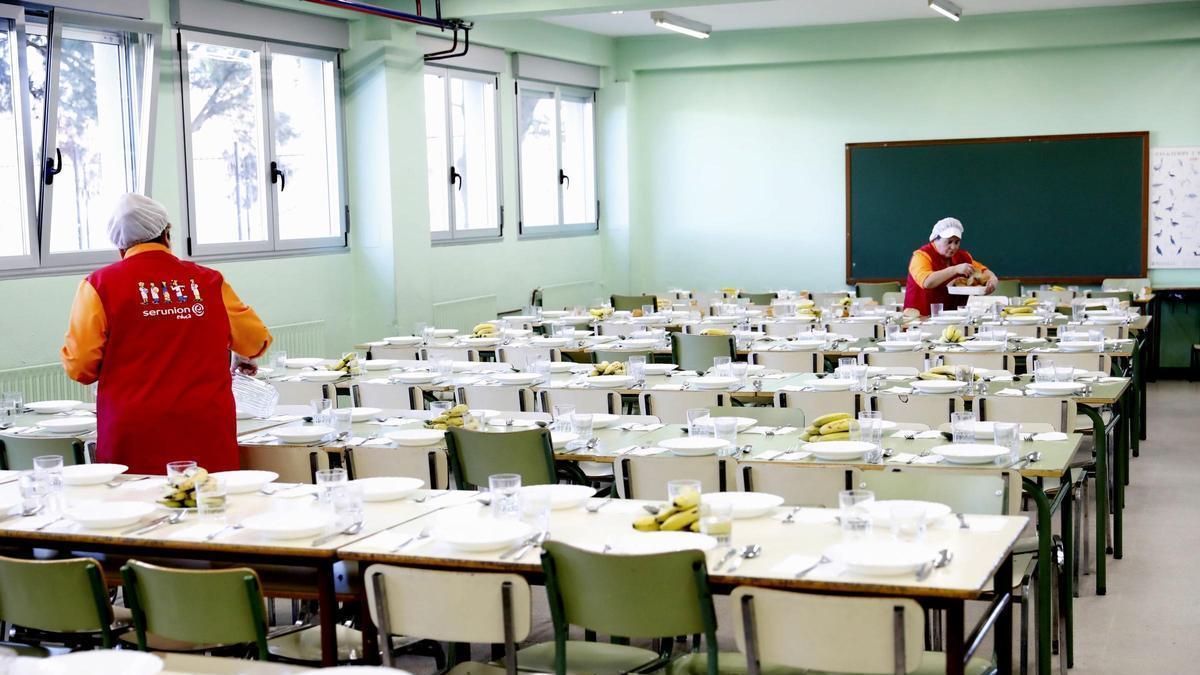 Personal prepara las mesas de un comedor escolar.