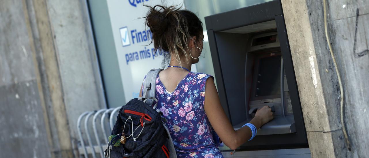 Una joven saca dinero en efectivo desde un cajero automático.