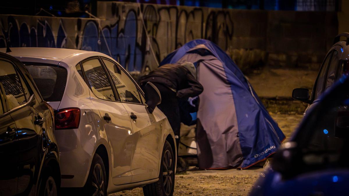 Una persona sin hogar entra en su tienda de campaña en un párking de Barcelona.