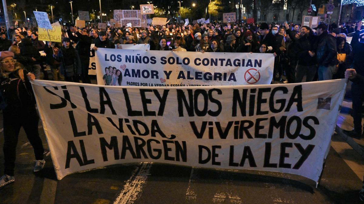 Los manifestantes sostienen pancartas que dicen &quot;los niños solo transmiten amor y alegría&quot;, &quot;si la ley nos niega la vida, viviremos fuera de la ley&quot;, durante una manifestación contra el pase de salud Covid-19, con el que las autoridades pretenden limitar la propagación del Pandemia Covid-19, en Barcelona , el 11 de diciembre de 2021. - Varios países de Europa y Asia han impuesto pasaportes vacunales para viajar o para acceder a determinados espacios públicos. (Foto de LLUIS GENE / AFP)