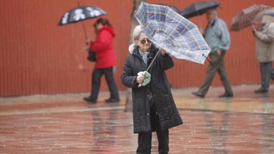 Una señora lucha contra el viento para colocar bien su paraguas en el centro de Málaga.