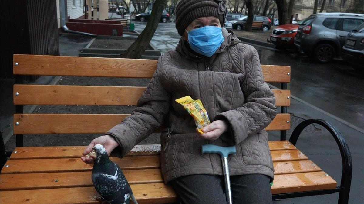 Una anciana protegida con mascarilla alimenta a una paloma en un banco cercano a su domicilio, en Moscú.