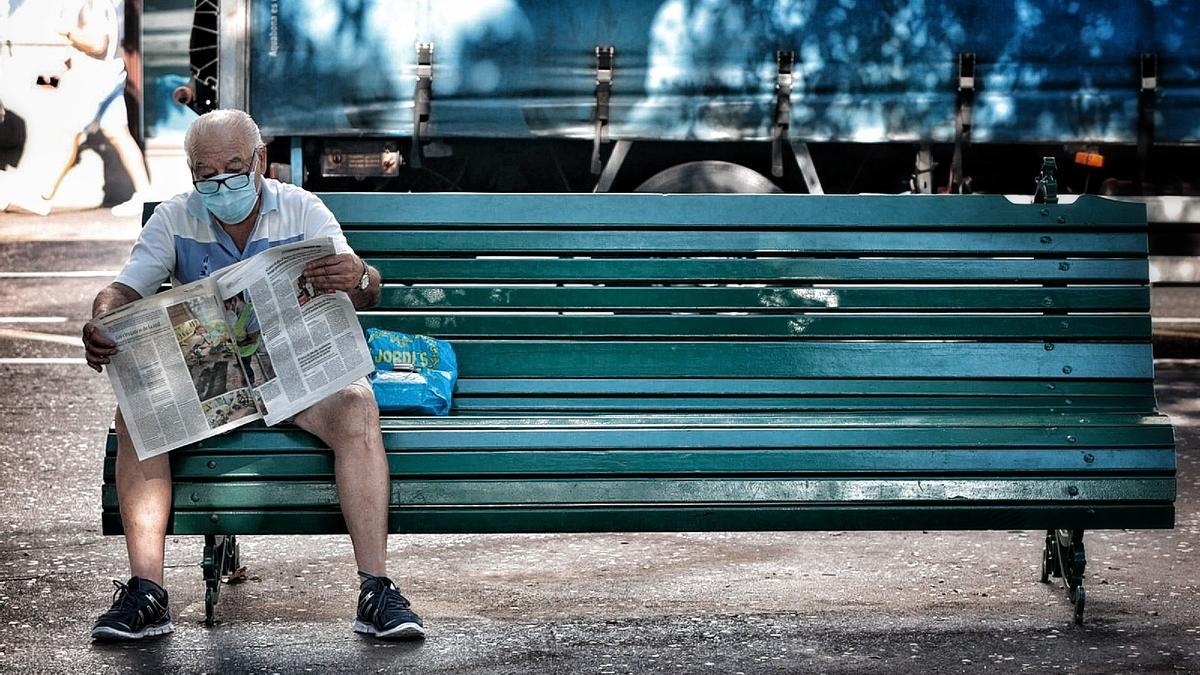 Un hombre con mascarilla lee el periódico en un banco de Santa Cruz de Tenerife.