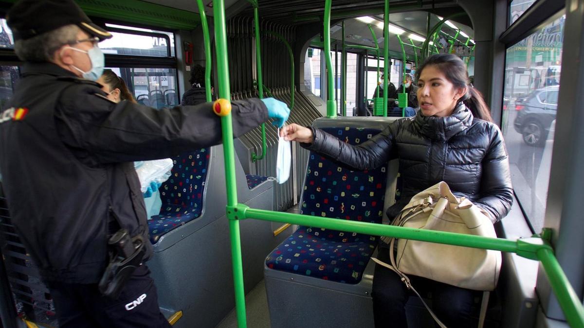 Un policía entrega una mascarilla a la pasajera de un autobús este lunes en Vigo.