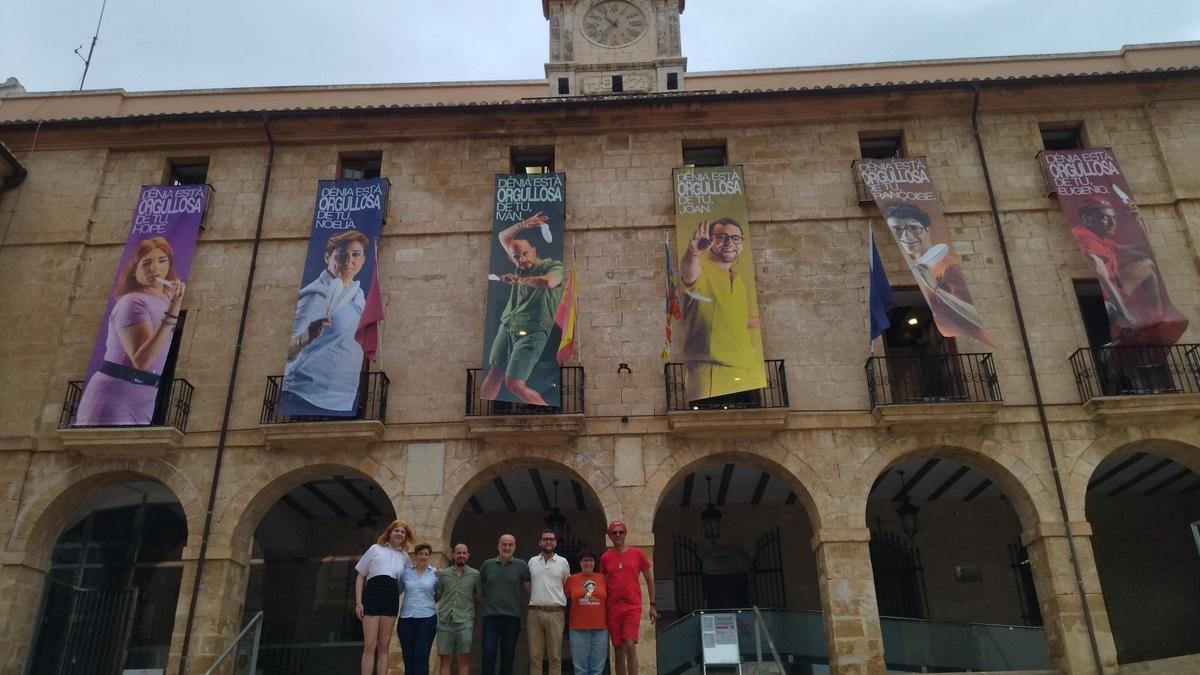 Hope, Noelia, Iván, Joan, Françoise y Eugenio, junto al concejal Javier Scotto, ante la fachada del ayuntamiento donde se ha desplegado la bandera arcoíris en primera persona