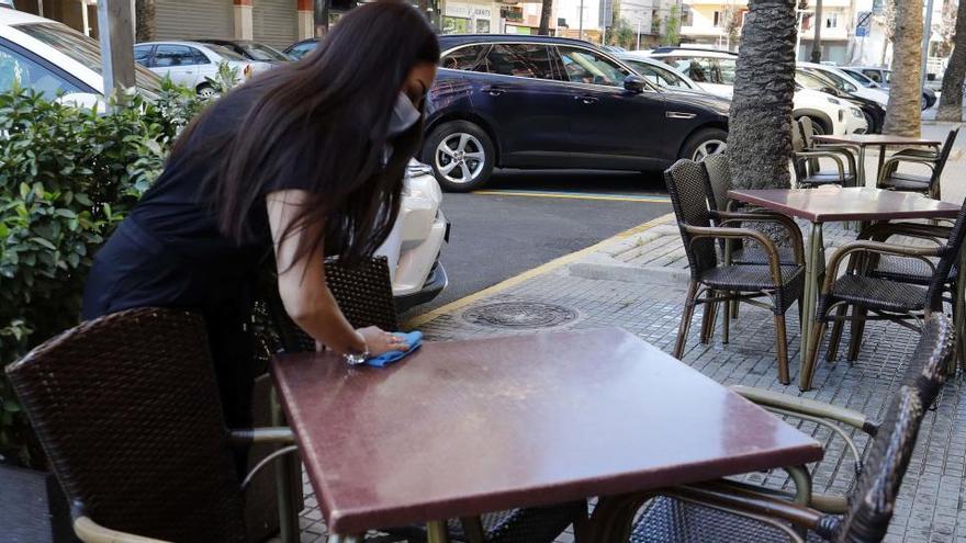 Una trabajadora desinfecta las mesas de una terraza.