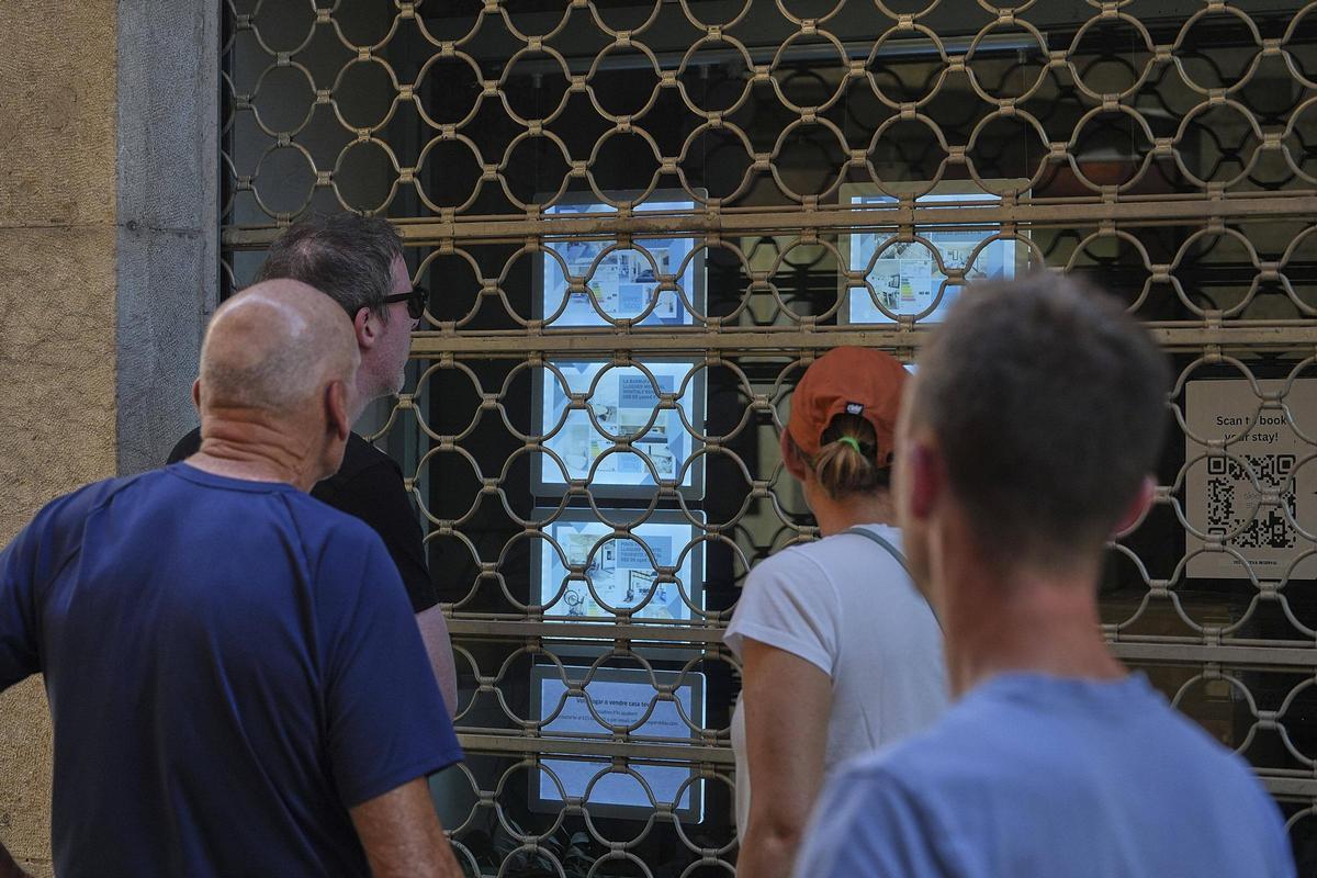 Turistes a Girona mirant anuncis de pisos turístics ahir a la tarda a l'aparador d'un establiment tancat.