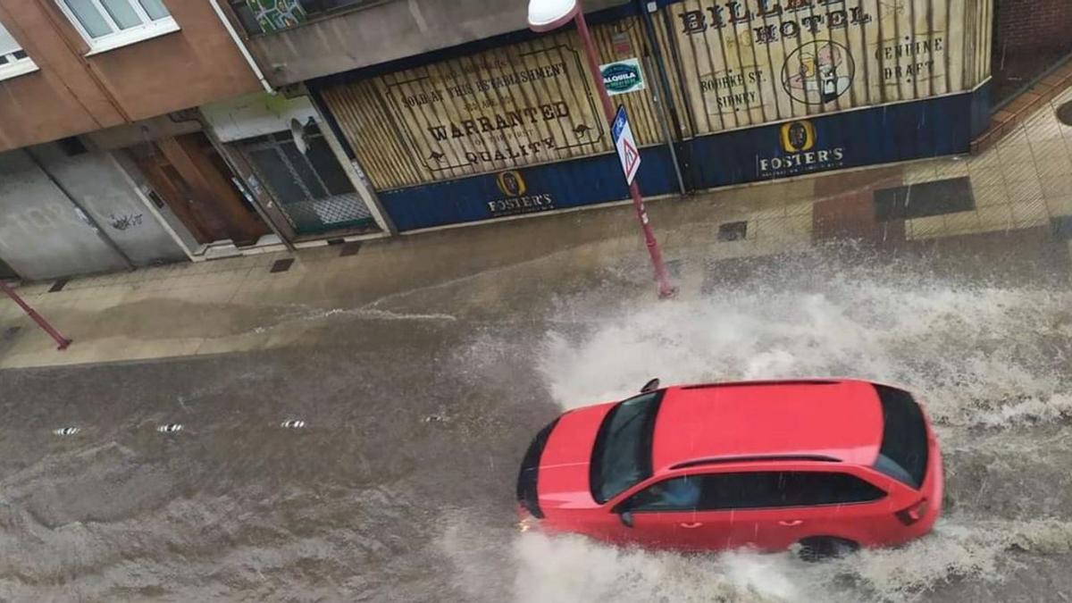 Un coche circulando por la calle Pelayo, en Pola de Laviana, anegada por el agua.