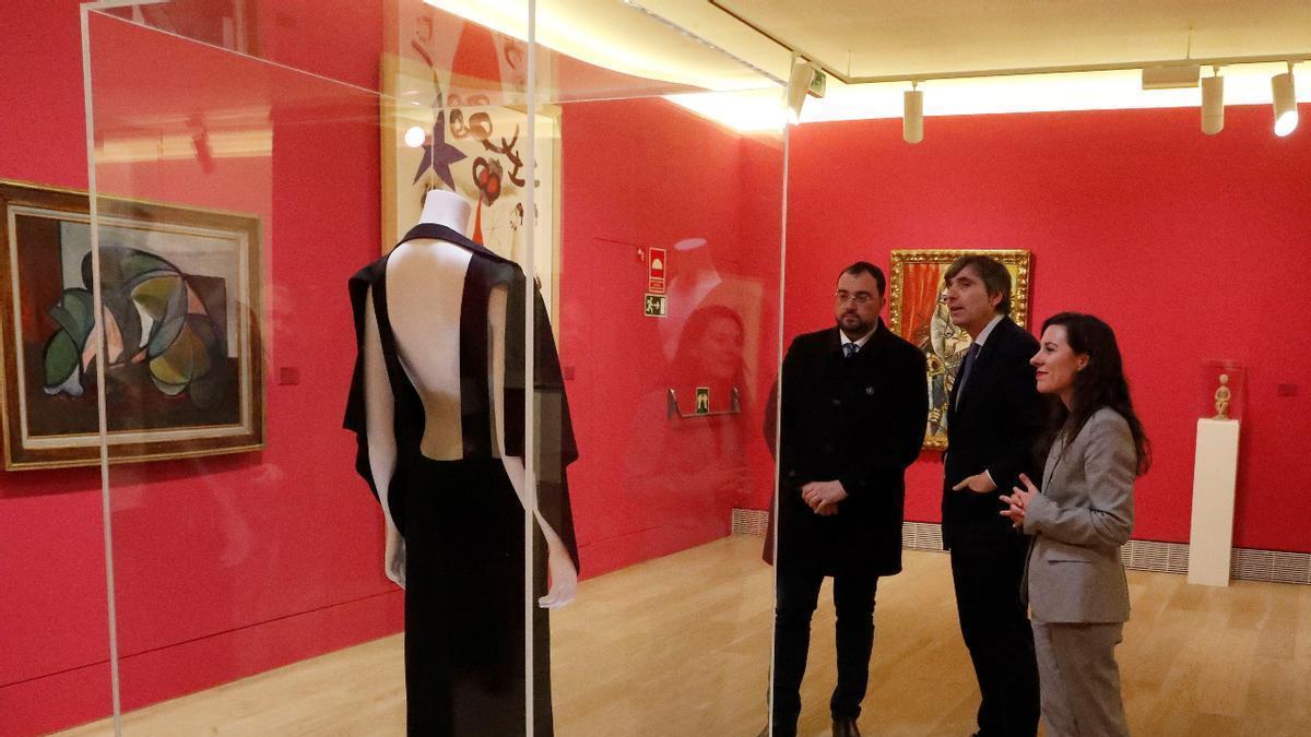 Adrián Barbón, Alfonso Palacio y Sara Moro, frente al vestido de Yves Saint Laurent, en el museo.