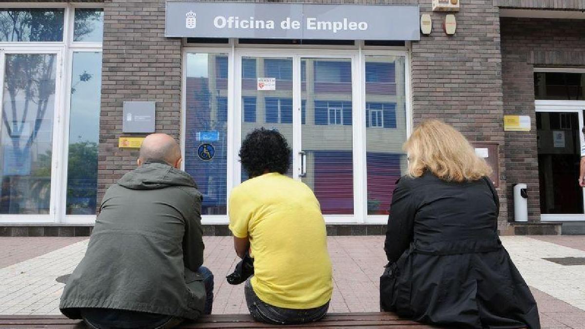 Tres personas descansan en un banco frente a una oficina pública de empleo de Santa Cruz de Tenerife.