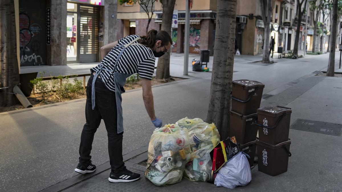 Un comerciante pone orden en sus residuos, en un alcorque frente a su establecimiento, en Gran de Sant Andreu