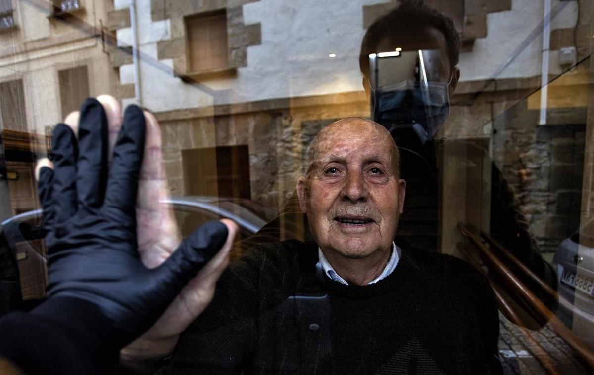 Visita al abuelo del fotógrafo, Miguel, de 90 años, durante el confinamiento. Ambos se saludan a través del cristal del portal, el 1 de abril del 2020.