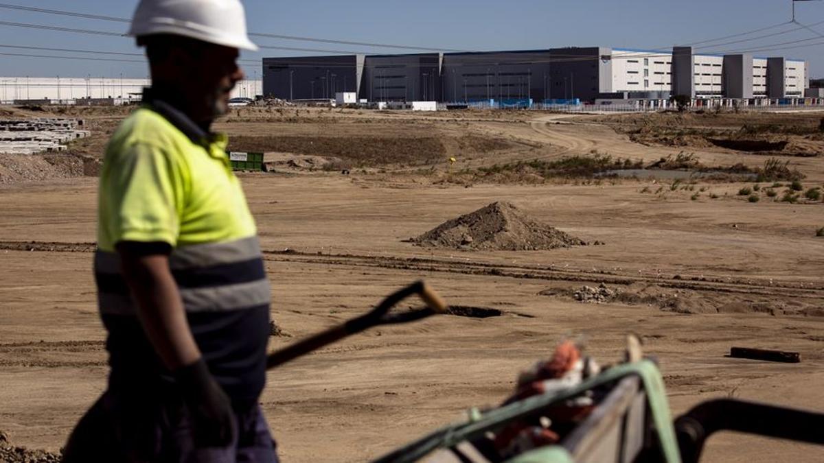 Un obrero trabaja en la urbanización del Puerto Seco de Illescas, con la nave de Amazon al fondo.