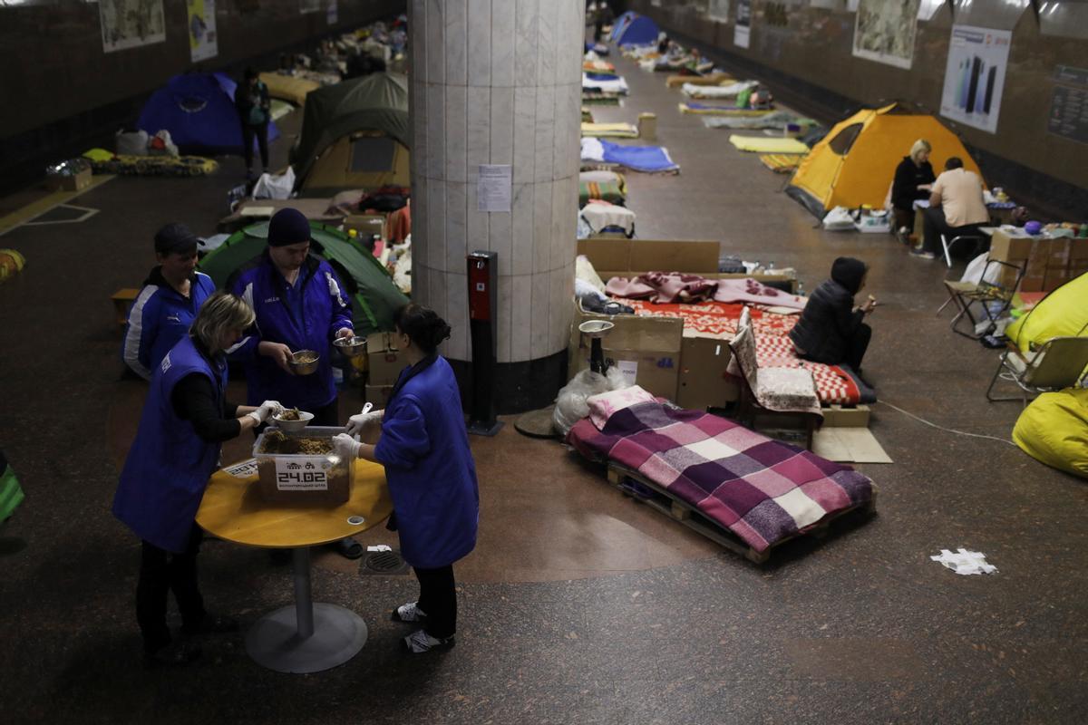 Las personas reciben alimentos distribuidos mientras los residentes encuentran refugio de los bombardeos en una estación de metro, en medio del ataque de Rusia contra Ucrania, en Kharkiv, Ucrania