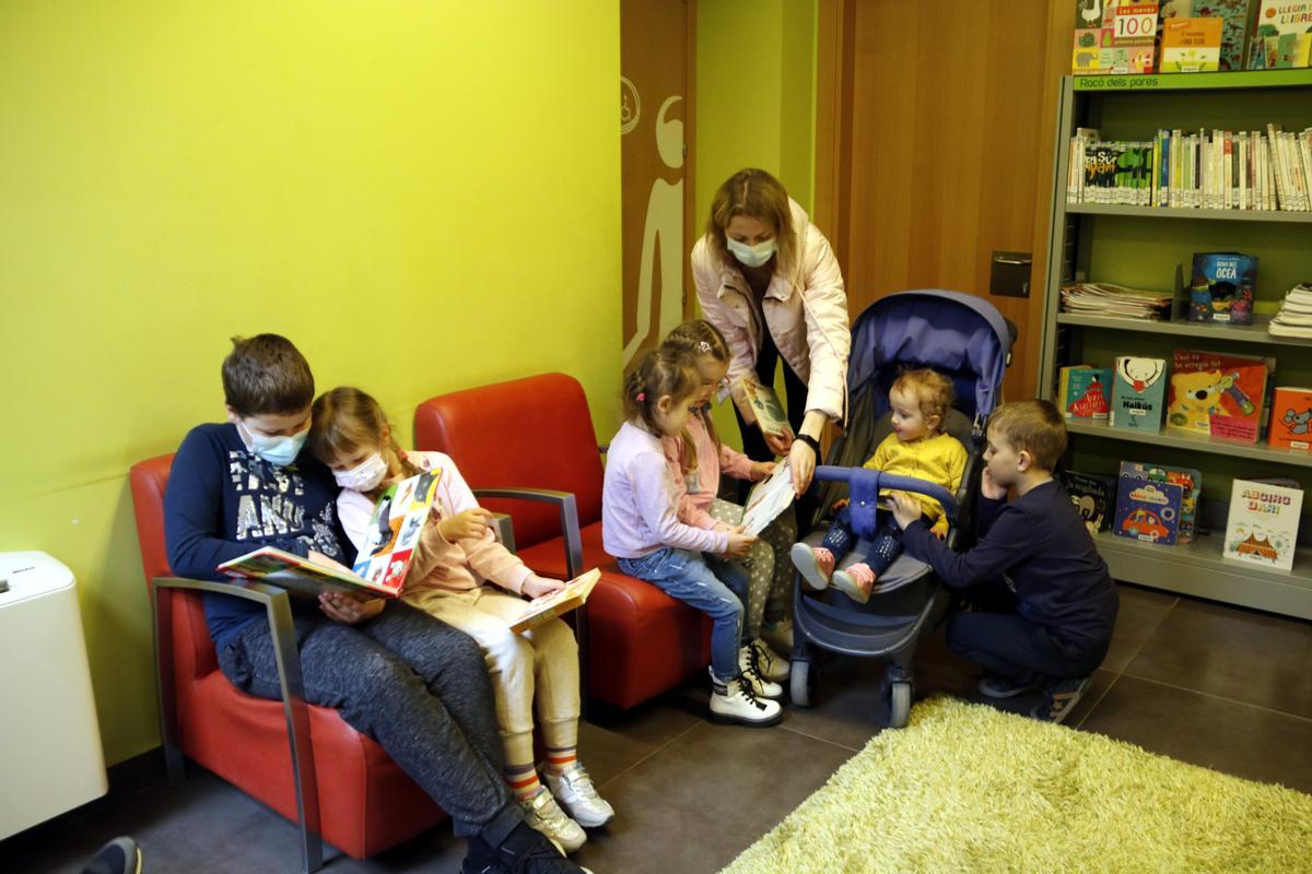 Niños recién llegados de Ucrania huyendo de la guerra en su país miran cuentos con la madre de uno de ellos en la biblioteca de Guissona.