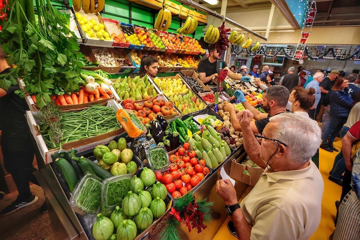 Varias personas adquieren alimentos en un puesto de un mercado de Canarias.