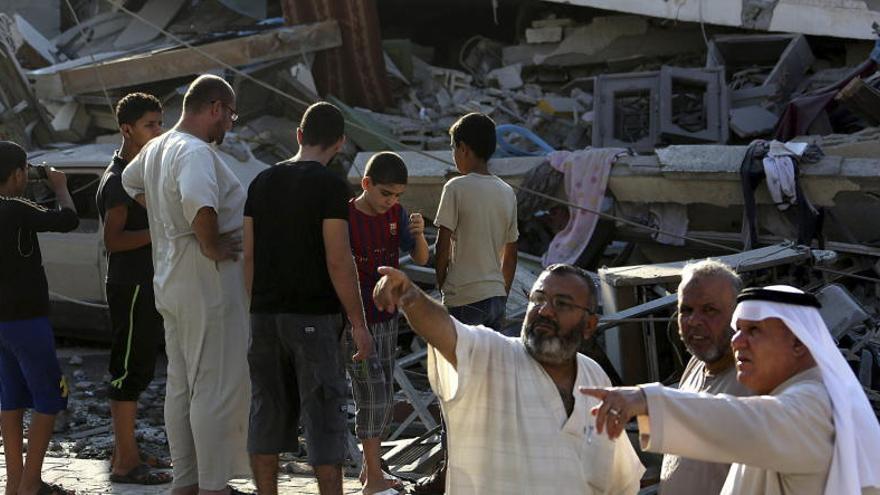 Unos palestinos miran un edificio destruído por proyectiles.