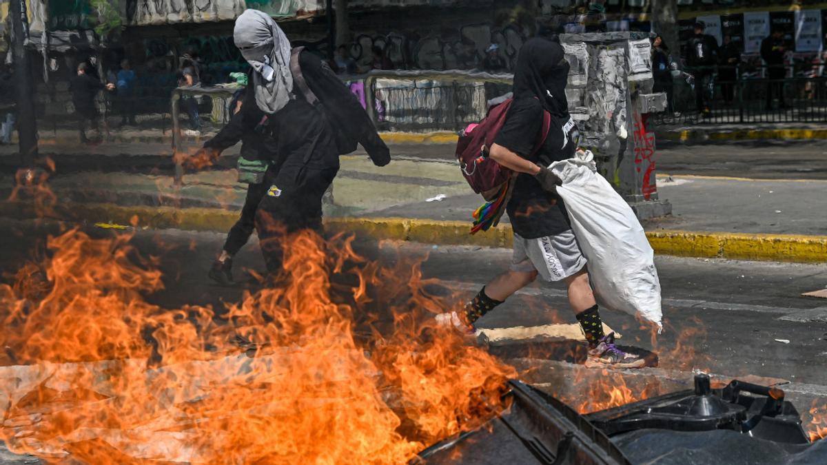 Demonstrators set a barricade on fire at the Baquedano square in Santiago, on the third anniversary of a social uprising against rising utility prices, on October 18, 2022. - The sustained movement forced then president Sebastian Pinera to increase tax spending and expand social programs, resulting in 2021 in the largest increase in public spending in the country's history at 33 percent. (Photo by Martin BERNETTI / AFP)