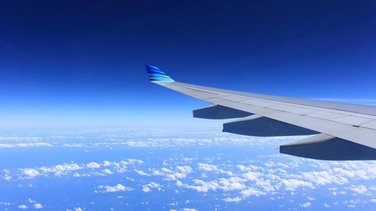 Un avión vuela sobre un cielo azul salpicado de nubes.