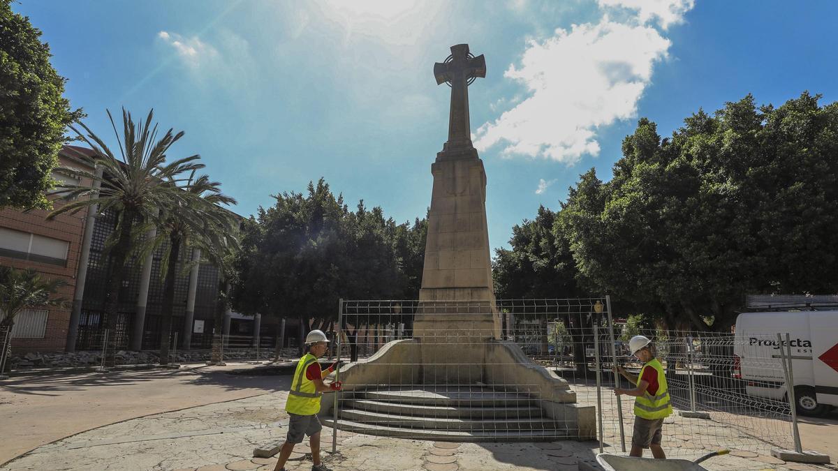 Operarios vallan la cruz de los caídos de Elche, para protegerla de las obras de la plaza