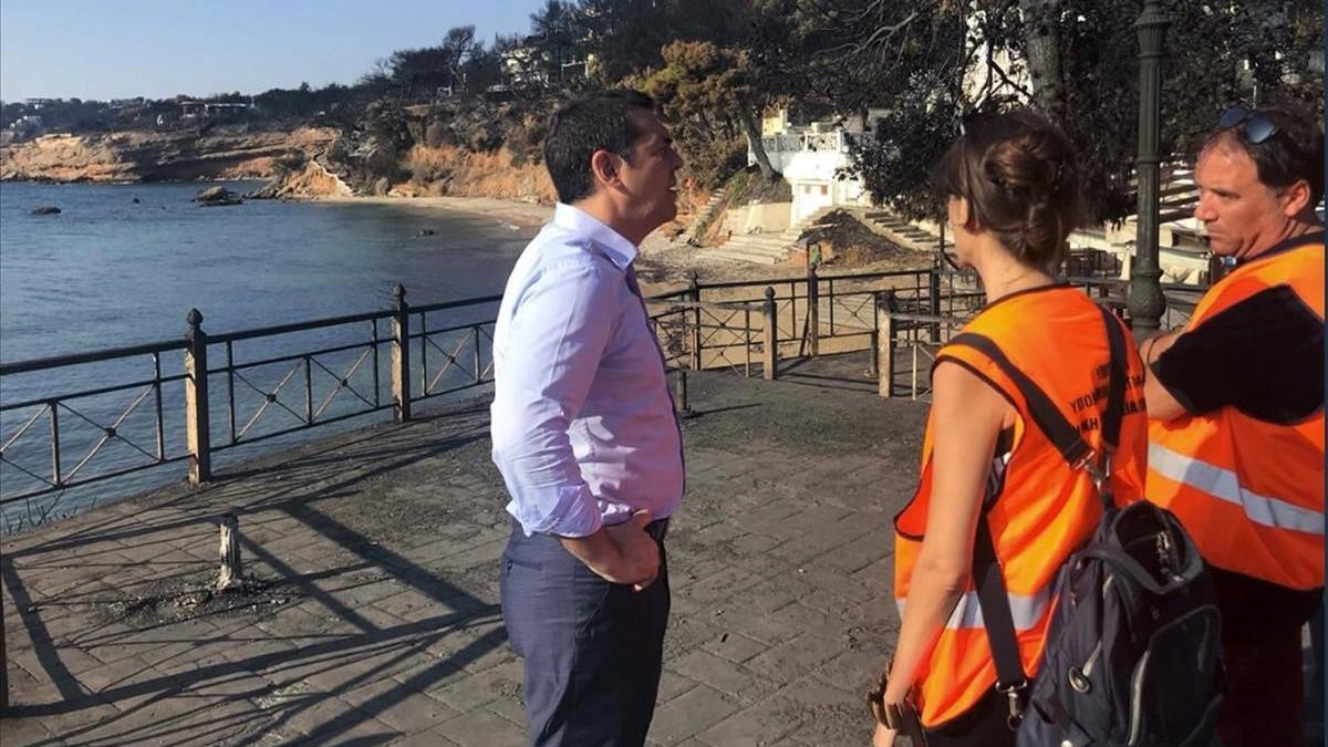 Tsipras habla con dos miembros de protección civil en Mati.