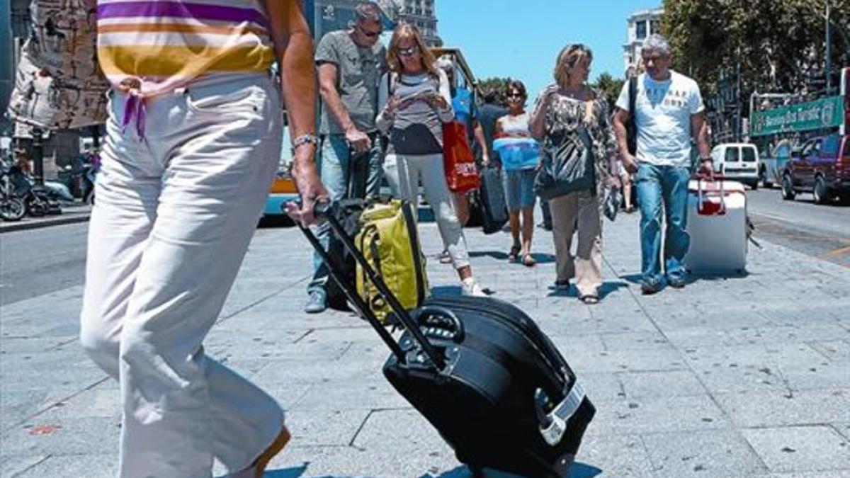 Turistas con maletas, recién llegados a la ciudad, o armados con plano para recorrerla, en la plaza de Catalunya, el pasado lunes.