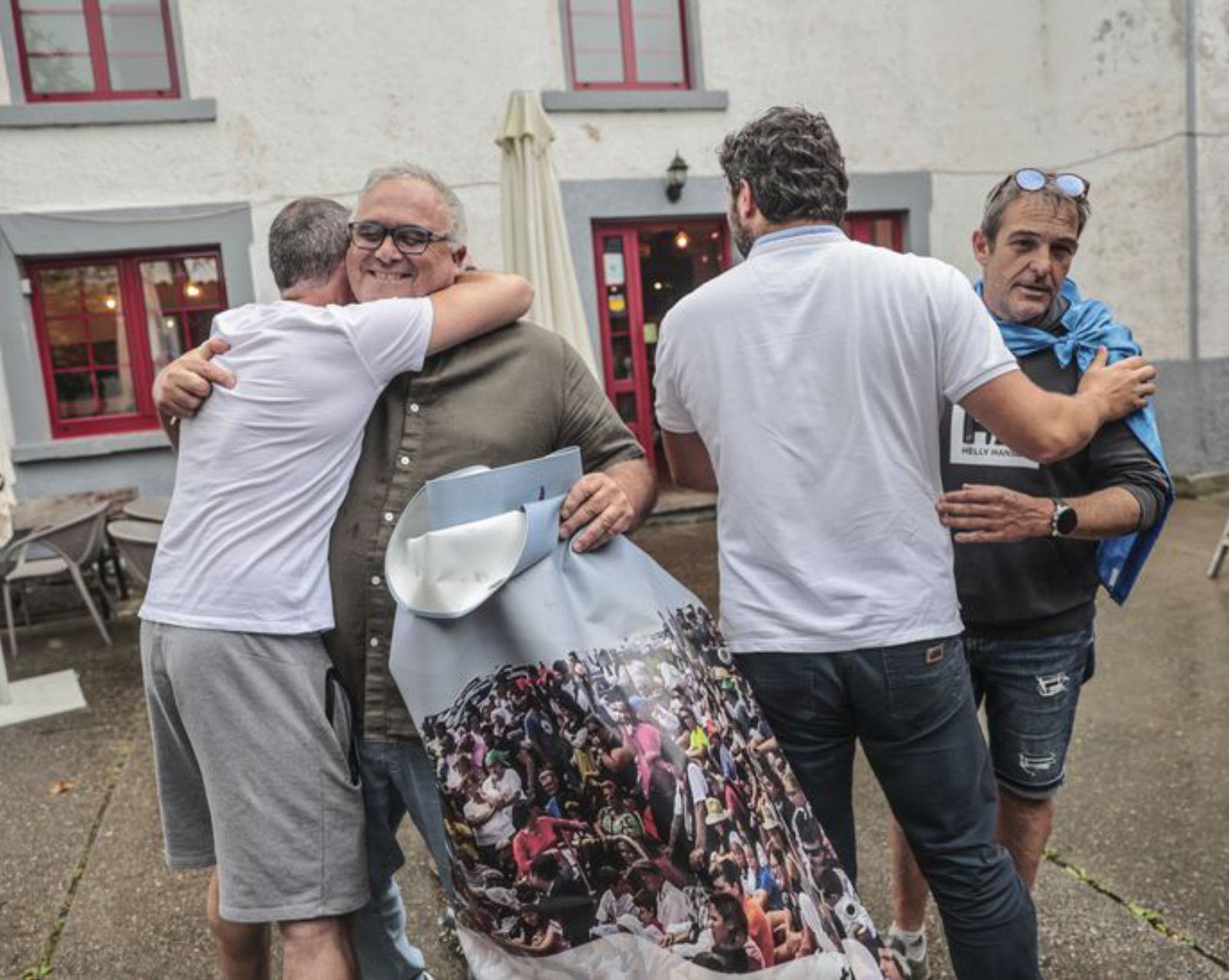 A la derecha, el presidente de La Regalina, Ángel Valverde, saluda al alcalde de Valdés, Óscar Pérez, de espaldas, en presencia de dos vecinos que se abrazan. | Irma Collín