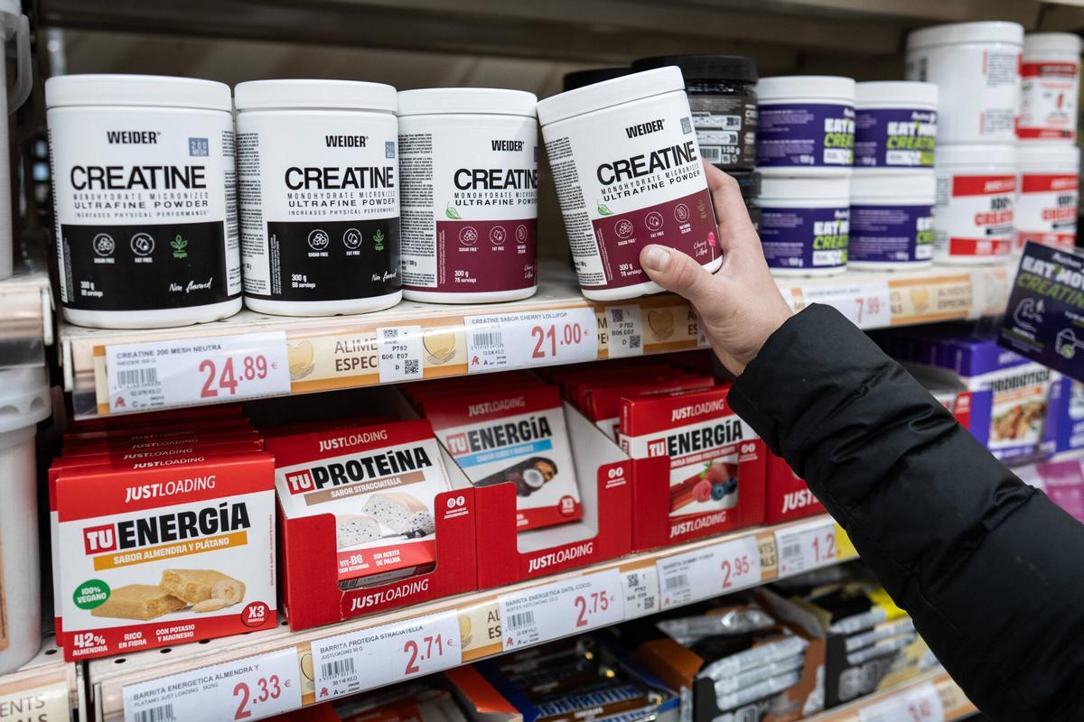 Un comprador compara diferentes marcas de creatina en un supermercado.